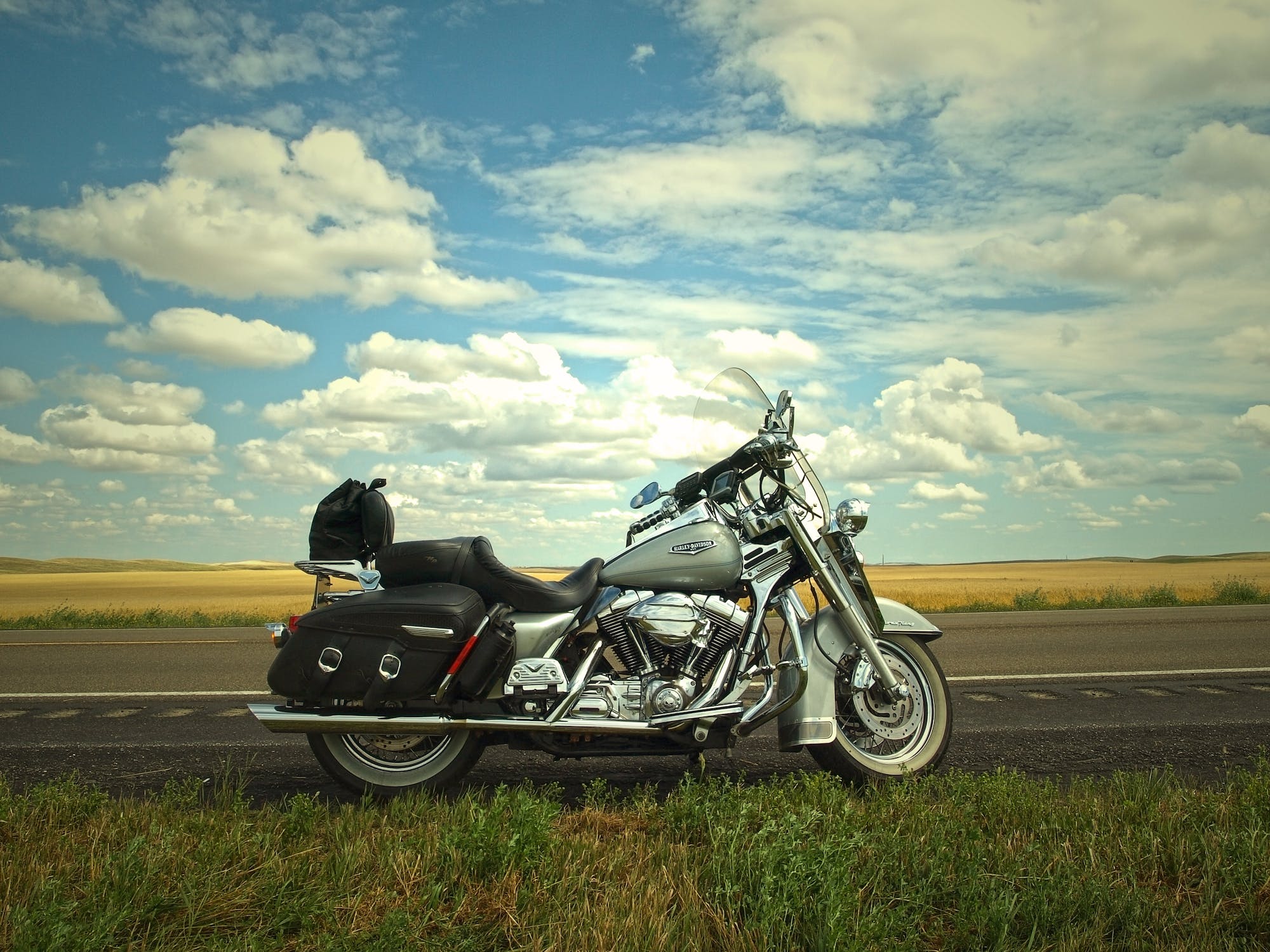 A gray and silver cruiser motorcycle parked on the side of a road near a green grass field.
