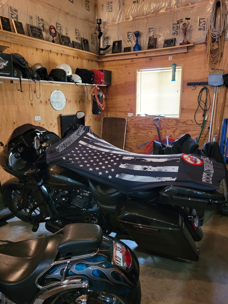 A side view of a black No Hot Azz motorcycle seat shade sun cover on a motorcycle in a garage featuring a black and white american flag.